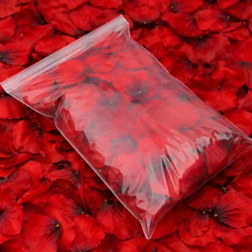 Clear plastic bag filled with red rose petals on a bed of red rose petals.